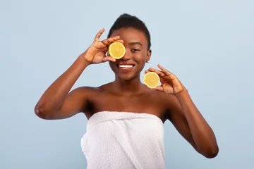 Foto op Canvas Excited african american lady with lemon halves in hands, posing wrapped in towel over blue background © Prostock-studio