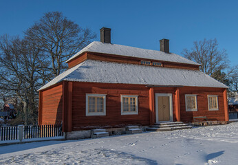 Old log house with snowy roof in a park on the island Djurgården a sunny and snowy winter day in Stockholm