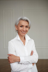 Portrait of an adult elderly self-confident woman with white hair looking at camera in white shirt...