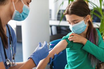 Schoolgirl Receiving Coronavirus Vaccine Injection Sitting With Doctor Indoor