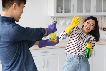 Playful asian lovers having fun while cleaning house together