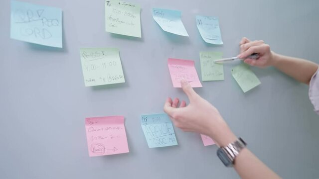 Close up female working hands using pen writing projects detail on the small sticky note paper on transparent glass board, meeting brainstorming presentation, mind mapping work organized, group ideas