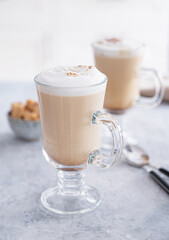 Two glasses of fragrant cappuccino coffee with cinnamon on a blue table against the background of a white kitchen in the early morning. Breakfast concept. Front view and close up