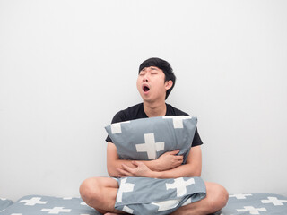 Asian man sit on the bed hug pillow feeling sleepy and yawn