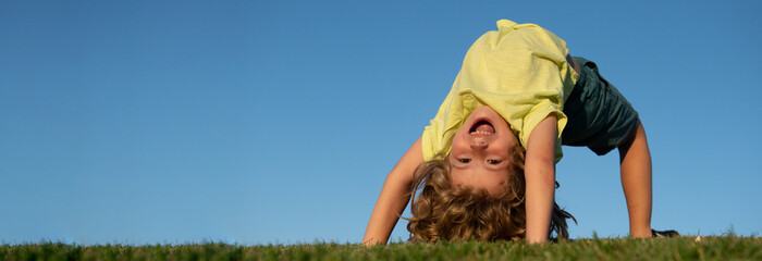 Banner with spring kids portrait. Excited little boy laying upside on the grass in the park. Outdoor portrait of pretty little boy on fresh green grass. Active healthy outdoor sport. Fun activity.