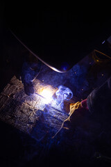A welder in a workshop with a welding machine, welds metal structures. A worker in a factory uses a welding mask, tools and metalworking equipment.