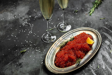 Red caviar filling metal plate and a glass of champagne on a stone background. Gourmet food close up, appetizer, selective focus, place for text