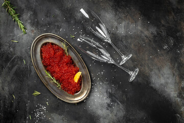 Red caviar filling metal plate and a glass of champagne on a stone background. Gourmet food close...