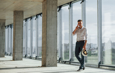 Walks and talks. Young man in formal wear is working indoors on the construction