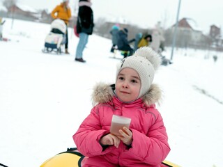 Little kid girl with a cup of warm cocoa outdoors for Christmas. Child on a walk in the city park. Family winter vacation.