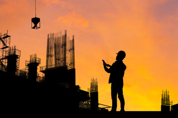Silhouette of Engineer man on building site, construction site at sunset in evening time.
