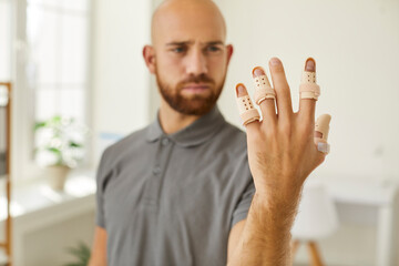 Orthopedic devices such as plastic splints on broken fingers of man's left hand. Close up of hand...