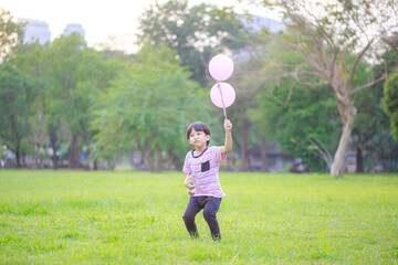A happy Asian child with colorful toy balloons outside the house. Smiling child having fun in green spring field on blue sky background. freedom concept