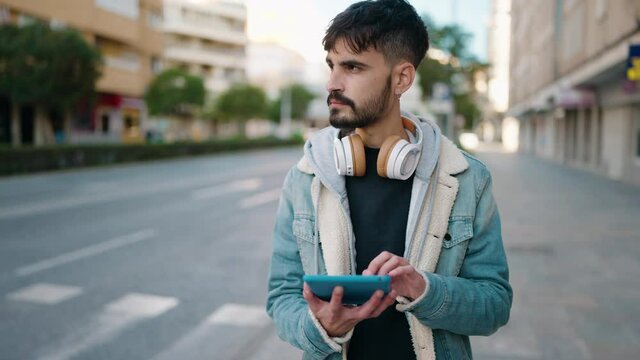 Young hispanic man wearing headphones using touchpad at street