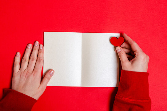 Blank postcard and female hands holding a heart on a red background for Valentine's Day