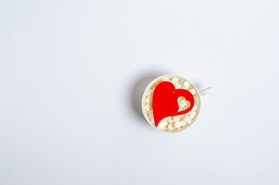 Wooden red heart in a cup with marshmallows on a white background with place for text.