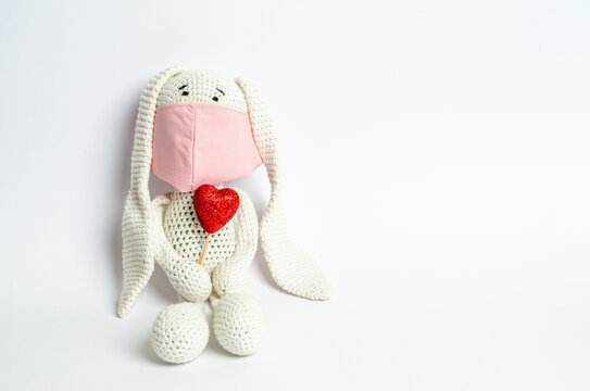 Soft toy bunny in a pink protective mask with a red shiny heart on a white background with a place for text