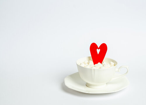 Cup with marshmallows and a red heart on a white background with place for text
