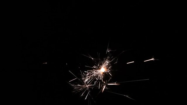 Full HD resolution slow-motion video. Close-up view of burning sparkler with many flying sparks on a black background. Holiday mood theme.