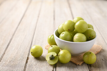Fresh Amla (Indian gooseberry) fruits in white bowl on wooden table.