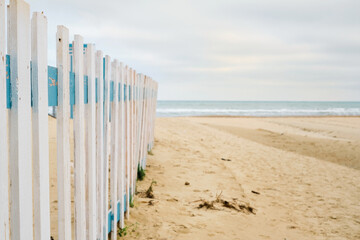 Deserted spring beach, fence in front of a public beach, cloudy sky in anticipation of rain. Off-season sea beach, place for text