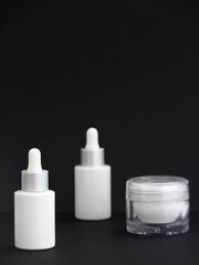 Blank serum dropper bottles mockup and lotion container in black background. Skincare daily routine for anti-aging and rejuvenation. Cosmetic packaging and branding for beauty products.