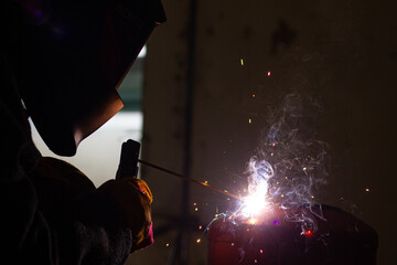 A welder in a workshop with a welding machine, welds metal structures. A worker in a factory uses a...