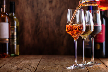 Red, white and rose wine in glasses on wooden background and collection of wine bottles, copy space