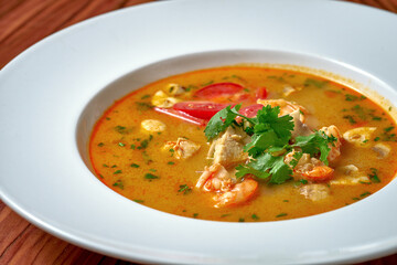 Asian soup tom yam with shrimps and chicken in a white plate on a wooden background