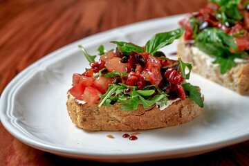 Bruschetta with sun-dried tomatoes and feta in a white plate on a wooden background