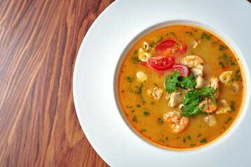 Asian soup tom yam with shrimps and chicken in a white plate on a wooden background