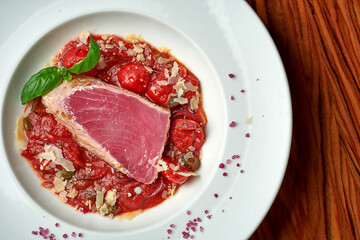 Tuna steak with stewed tomatoes in white plate on wood background