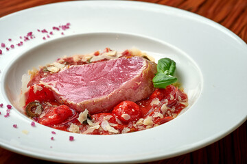 Tuna steak with stewed tomatoes in white plate on wood background