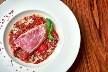 Tuna steak with stewed tomatoes in white plate on wood background