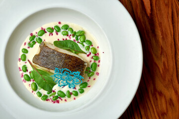 Black cod fillet with edem beans and white sauce in a white plate on a wooden background