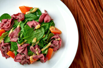 Salad with roast beef and pumpkin in a white plate.