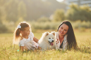 Laying down together. Woman and little girl have a walk with dog on the field at sunny daytime