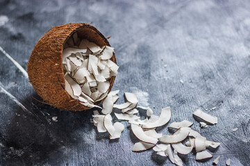 healthy snack: home made roasted coconuts chips in coconut bowl on dark background. Vegan. Clean eating. Plant based.