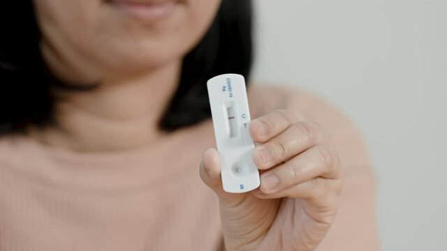 A long-haired Asian woman in a brown suit has used a rapid antigen test kit for self-test the COVID-19 epidemic at home and has shown a negative result of no COVID-19, showing 1 red line.