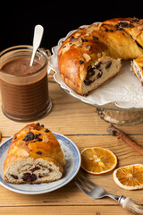 Top view of cut chocolate brioche, on wooden table with glass of chocolate and orange slices, vertical, black background