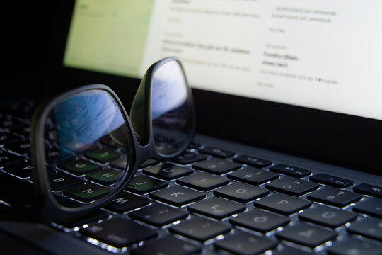 Home office, Close-up of an illuminated laptop keyboard on which a pair of glasses is lying. The screen is reflected in the glasses.