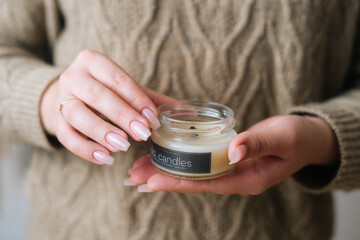 Close-up cropped shot of unrecognizable young woman holding scented handmade candle in glass jar...