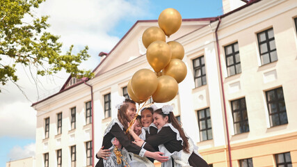 Cheerful Russian girls graduating with orange balloons on the last school day.