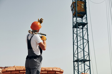 With crane at background. Young construction worker in uniform is busy at the unfinished building