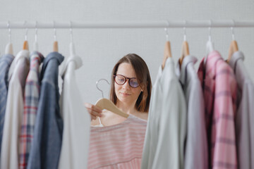 a European woman professional stylist with dark hair and glasses chooses clothes for a business meeting or dinner. millennial housewife woman disassembles home wardrobe for washing or recycling. a