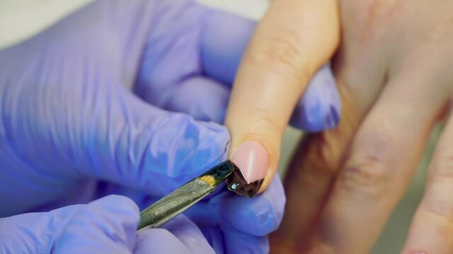close-up of a manicurist paints a black French on the client's nails with a brush.