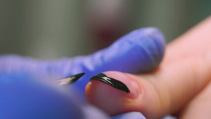 close-up of a manicurist paints a black French on the client's nails with a brush.