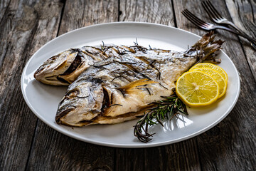 Roast sea bream with rosemary and lemon on wooden table
