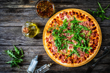 Circle pizza with mozzarella, pork ham and arugula on wooden table
