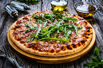 Circle pizza with mozzarella, pork ham and arugula on wooden table
